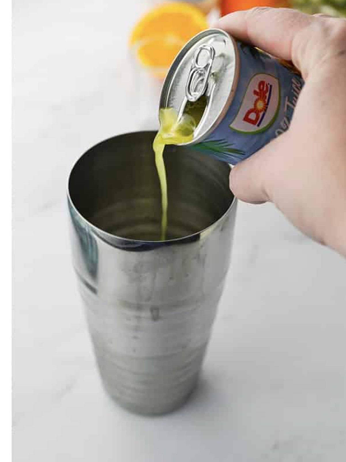 Pouring pineapple juice from a can into the cocktail shaker.