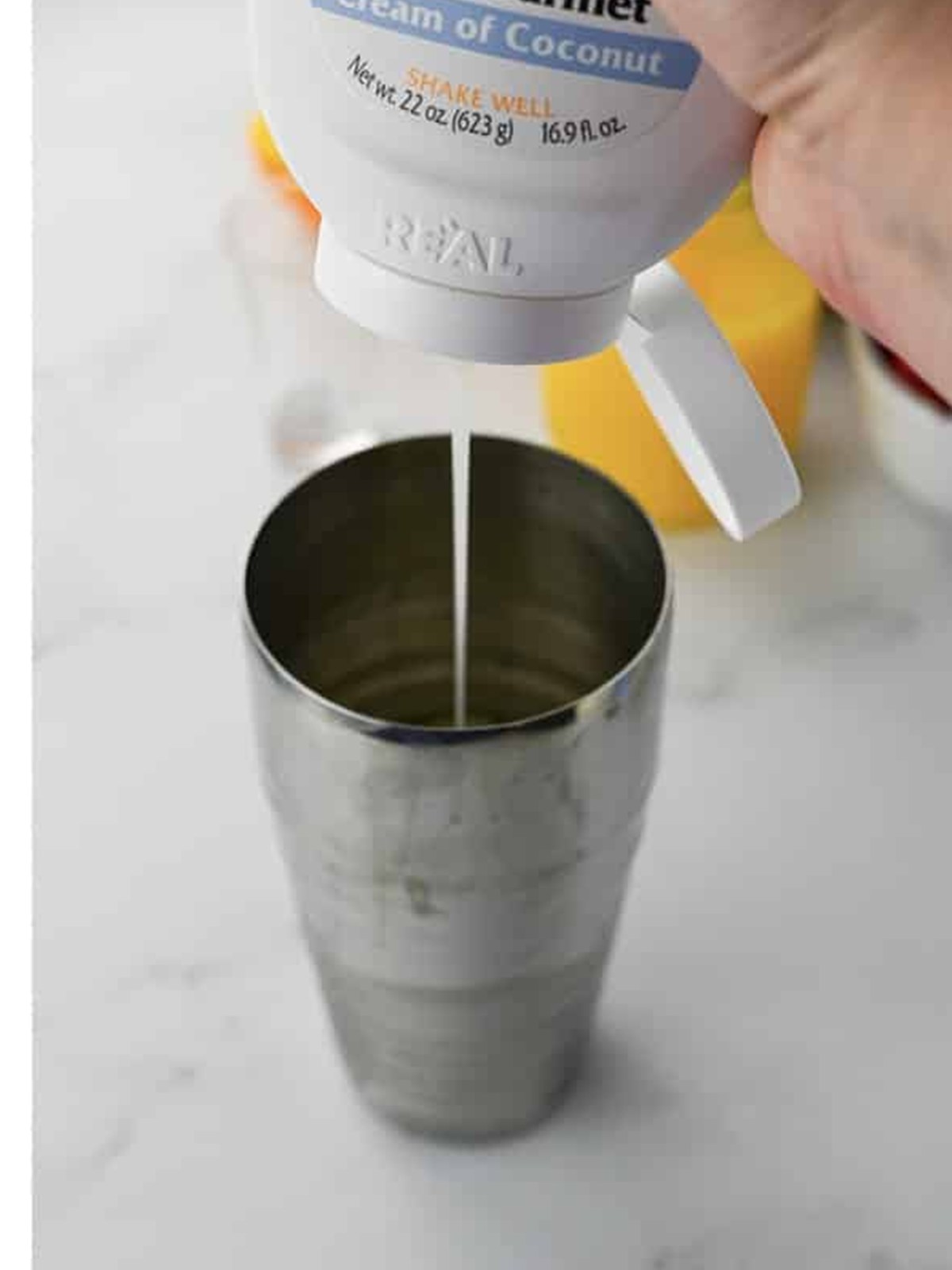 Squeezing cream of coconut into the cocktail shaker to finish the painkiller cocktail mix.