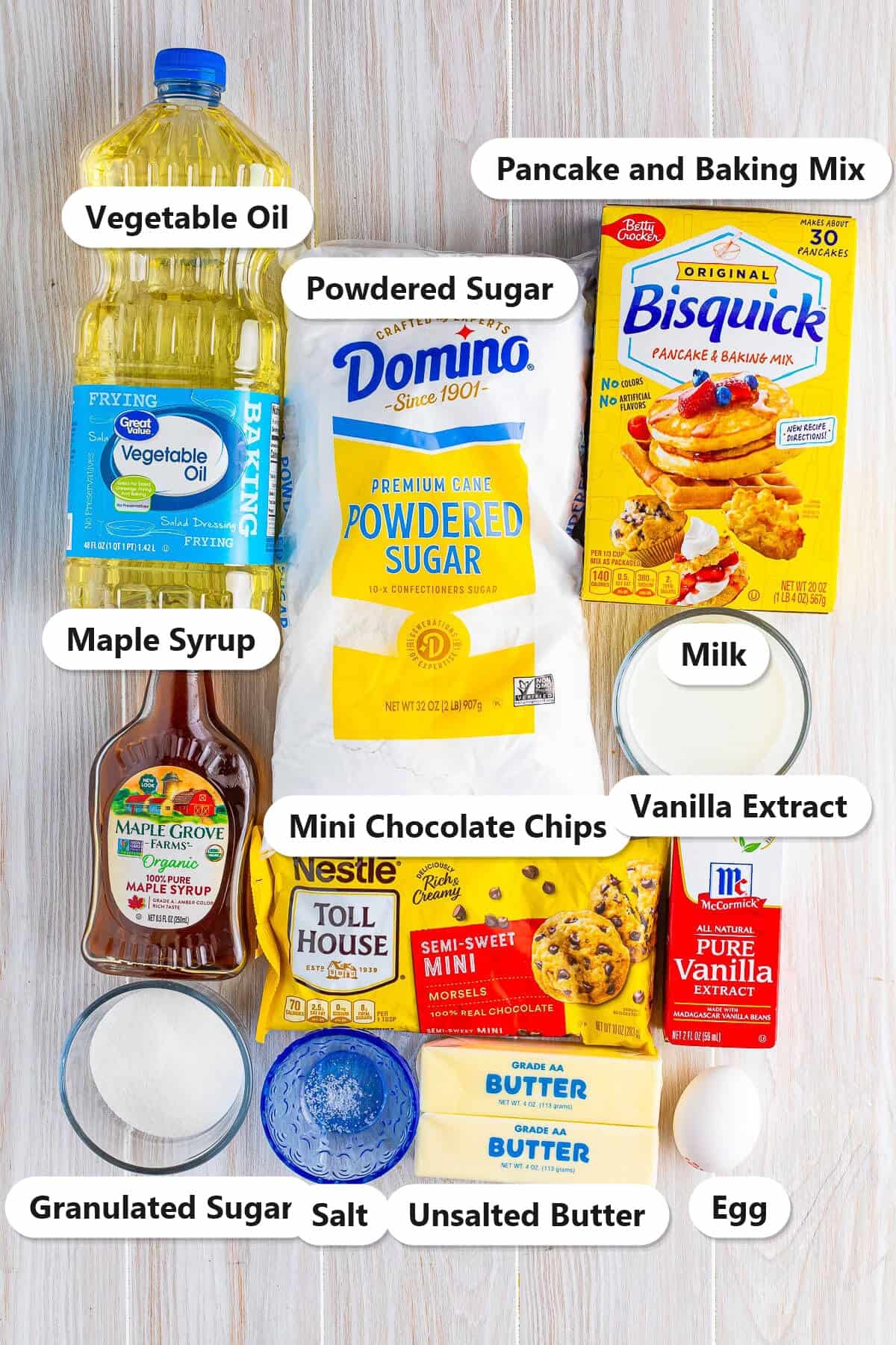 Labeled ingredients for pancake cupcakes including pancake and baking mix, maple syrup, mini chocolate chips, milk, egg, vegetable oil, butter, powdered sugar, and vanilla.
