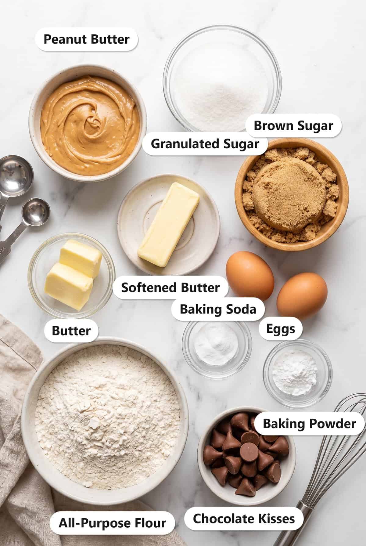Labeled ingredients for Peanut Butter Blossoms including peanut butter, sugar, brown sugar, butter, eggs, flour, baking soda, baking powder, and chocolate kisses.