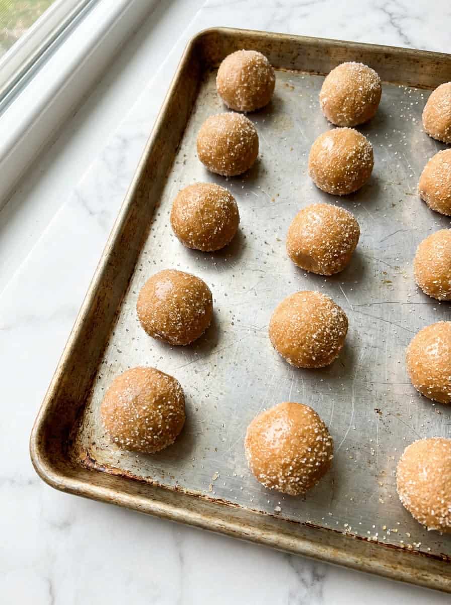 Peanut butter cookie dough balls rolled in granulated sugar on a cookie sheet.
