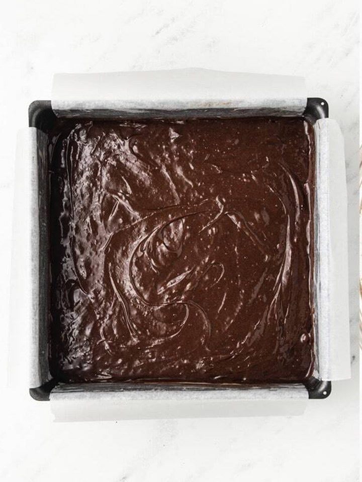 Brownie batter smoothed into a parchment lined square baking pan.