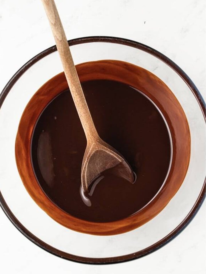 Melted dark chocolate and butter stirred glossy in a glass bowl for the brownie layer.