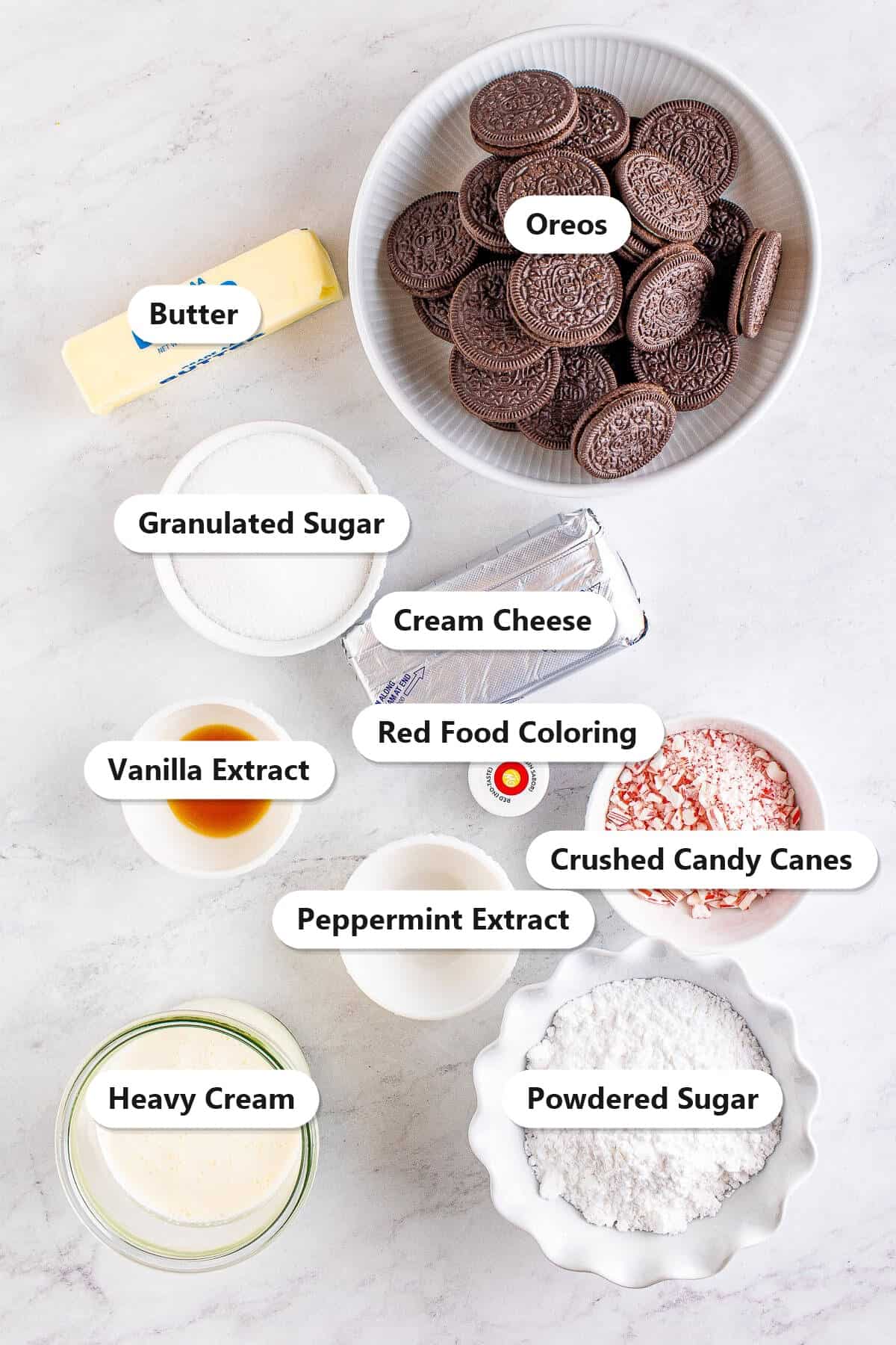 Labeled ingredients for peppermint cheesecake including Oreos, butter, cream cheese, sugars, heavy cream, peppermint extract, crushed candy canes, and red food coloring.