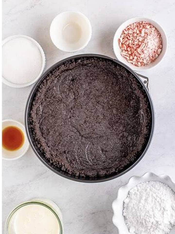 Oreo crust pressed into the bottom and sides of a springform pan for peppermint cheesecake.