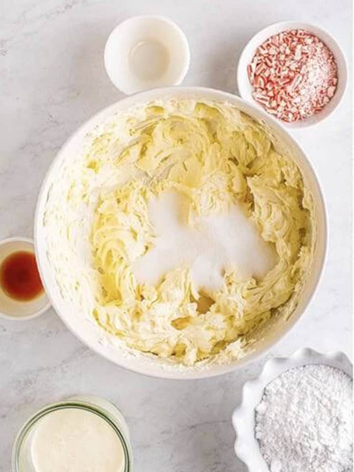 Cream cheese whipped smooth in a bowl with granulated sugar added for peppermint cheesecake filling.