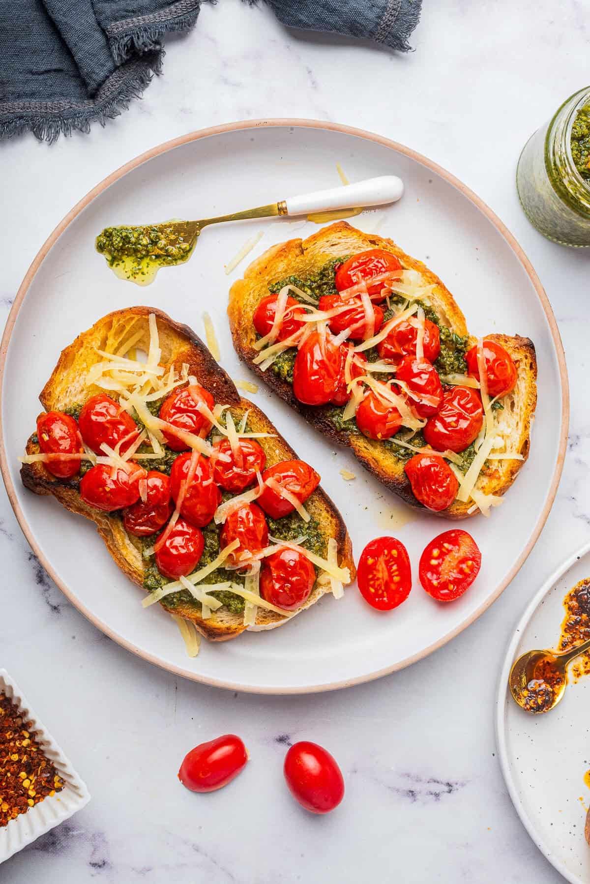 Two slices of Pesto Toast with cherry tomatoes and parmesan served on a plate.