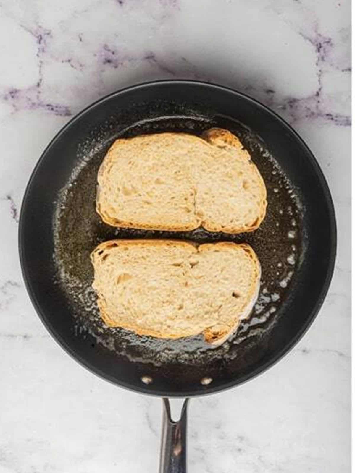 Placing slices of rustic bread into a skillet with melted butter to toast.