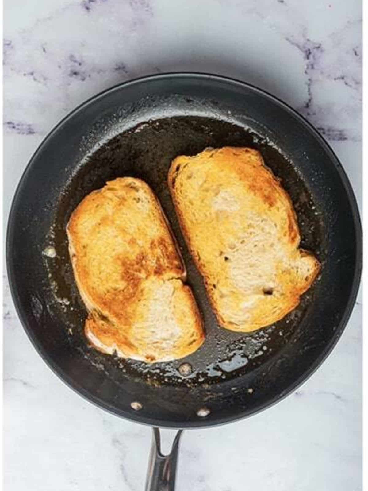 Bread slices toasted golden brown and crispy in a skillet for Pesto Toast.