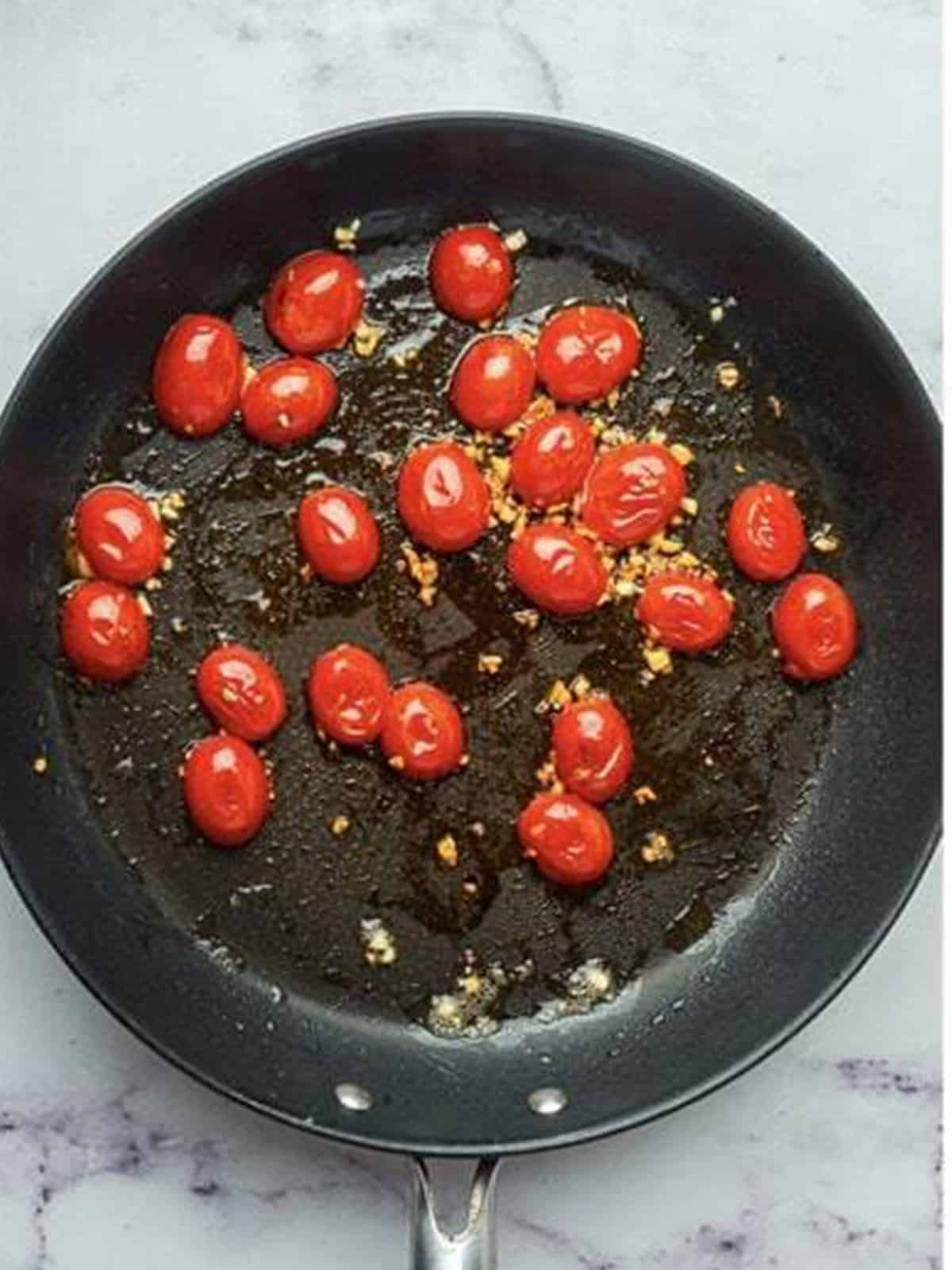 Cooking halved cherry tomatoes in the skillet until softened and wrinkled.