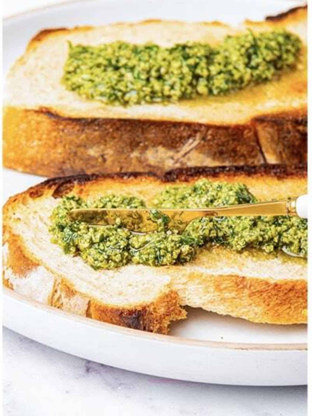 Spreading a layer of pesto over the toasted bread slices.