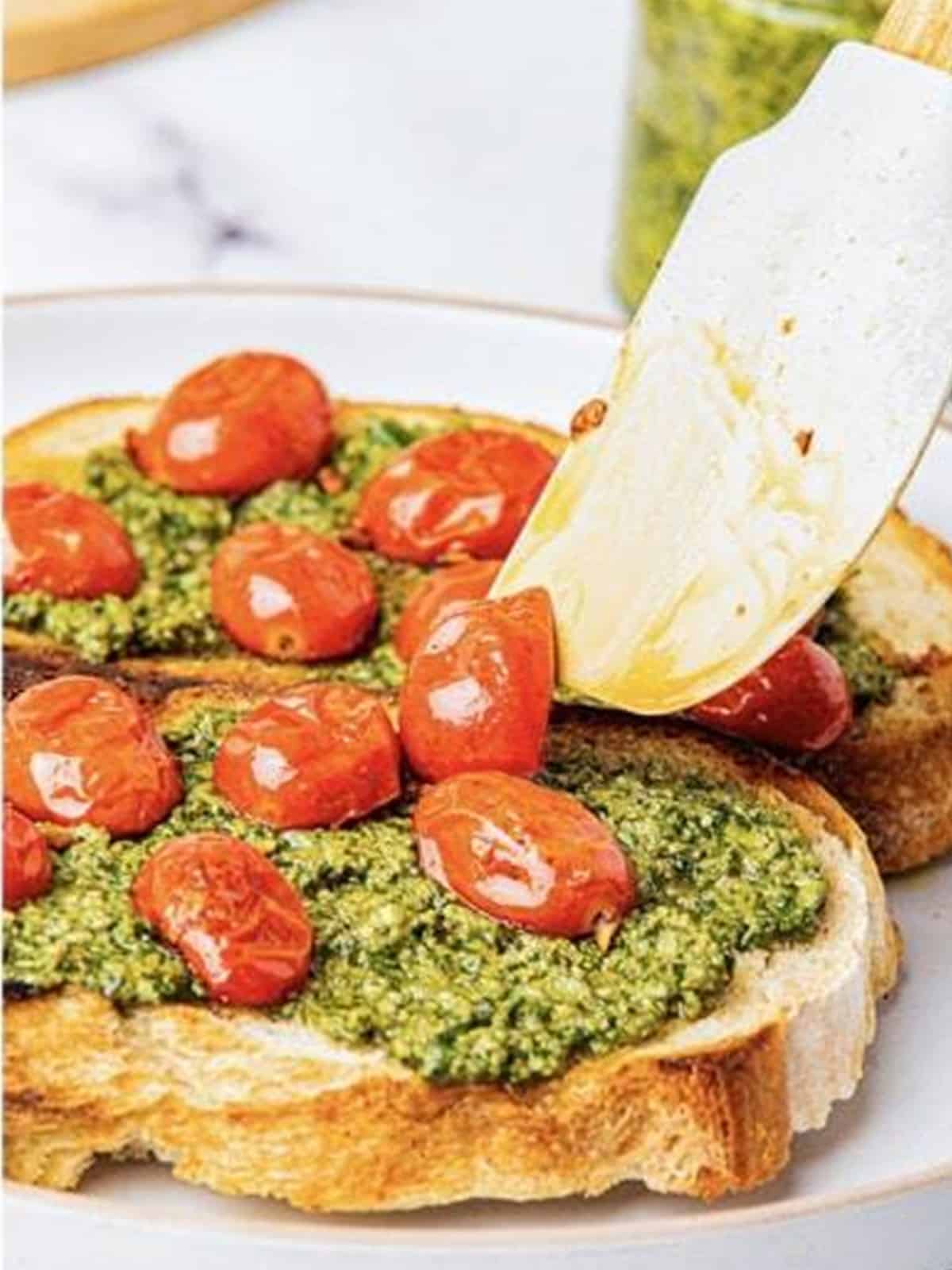 Topping the pesto toast with sauteed cherry tomatoes and grated parmesan cheese.