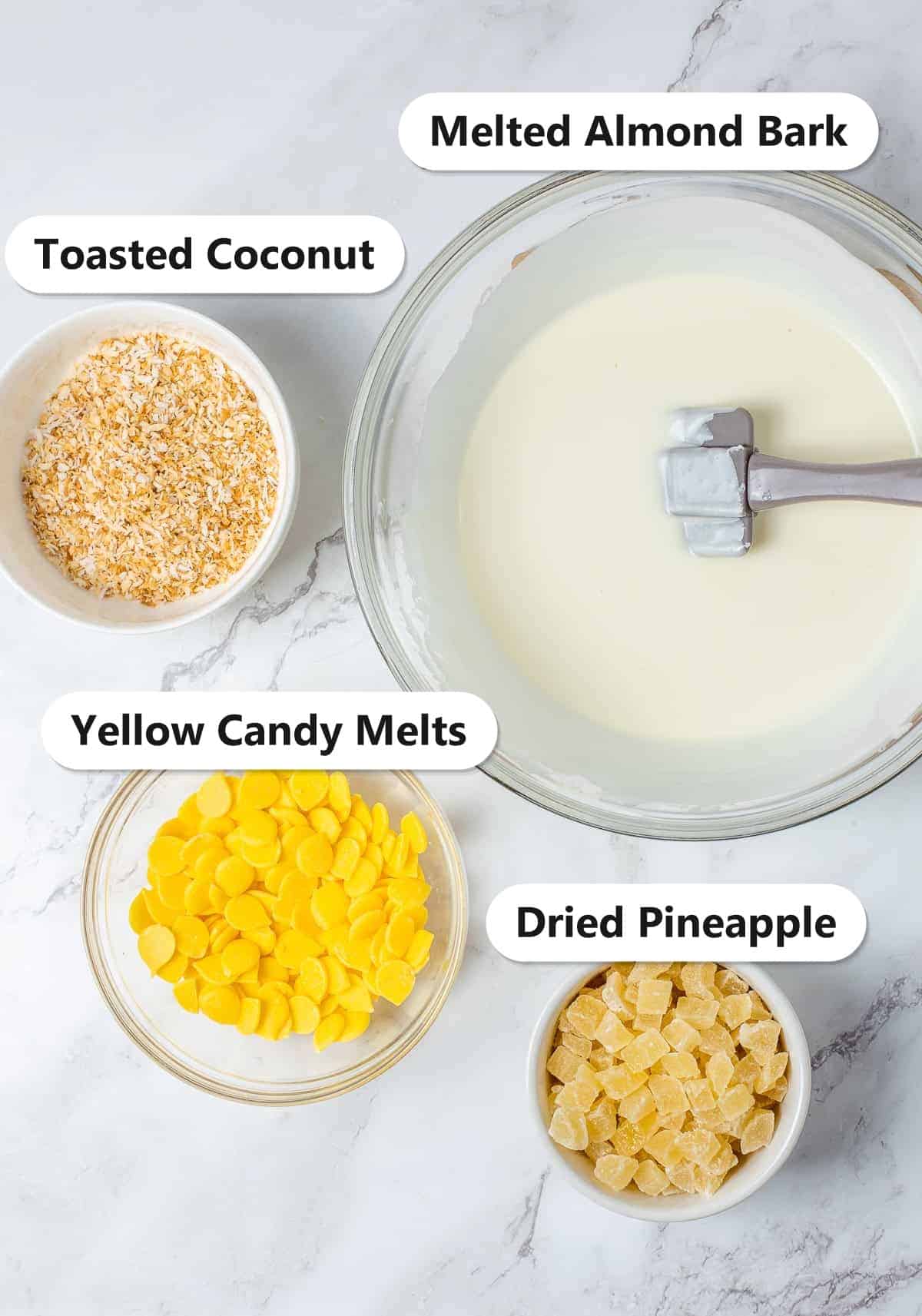 Labeled ingredients for pina colada bark including melted almond bark, toasted coconut, yellow candy melts, and dried pineapple.