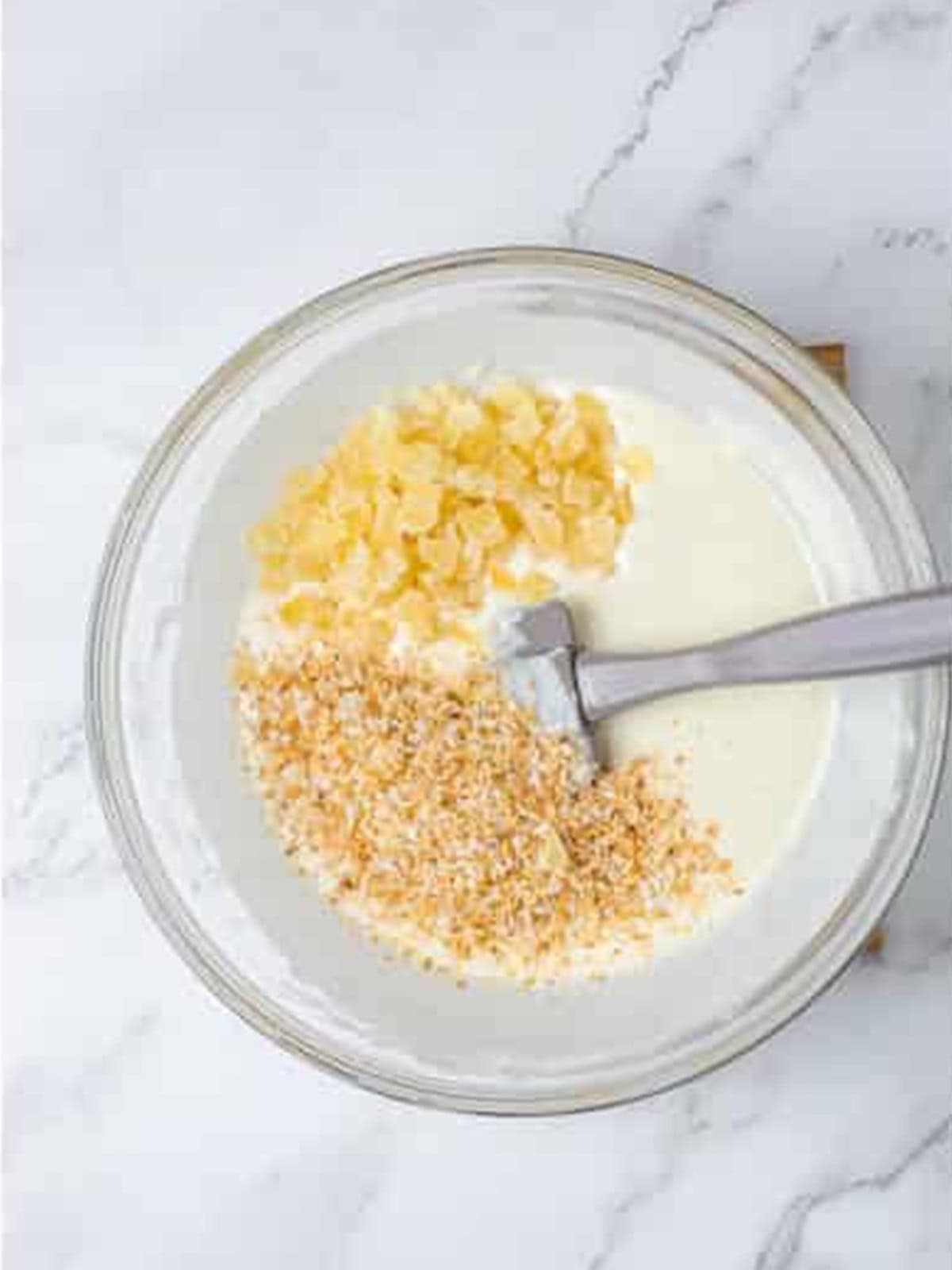 Dried pineapple and toasted coconut added to a bowl of melted almond bark.