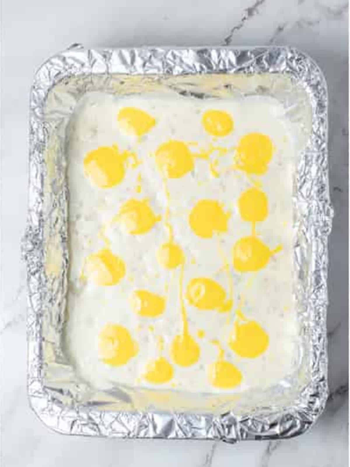 Yellow candy melt dollops dotted over the white bark layer in a foil lined pan.