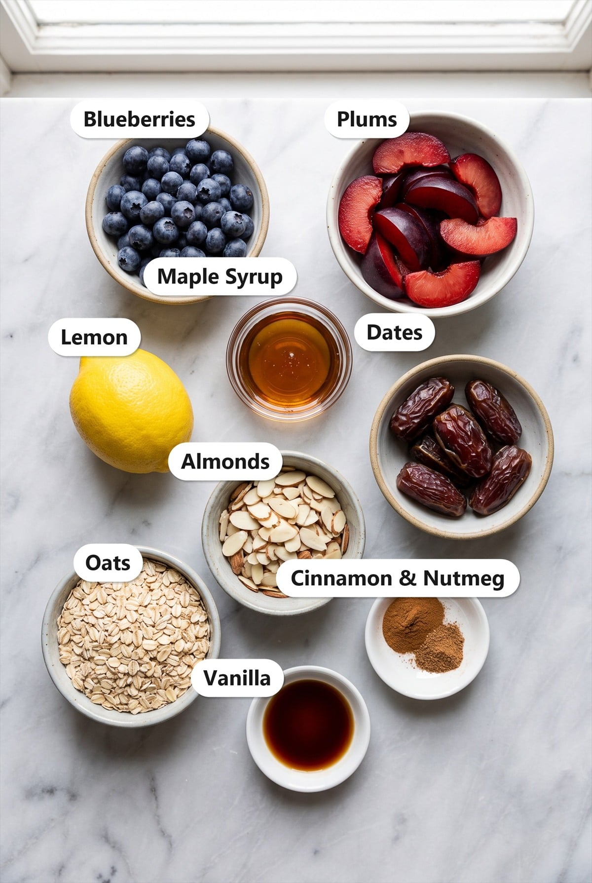 Labeled ingredients for no bake plum crumble including blueberries, plums, maple syrup, lemon, dates, sliced almonds, oats, cinnamon, nutmeg, and vanilla.