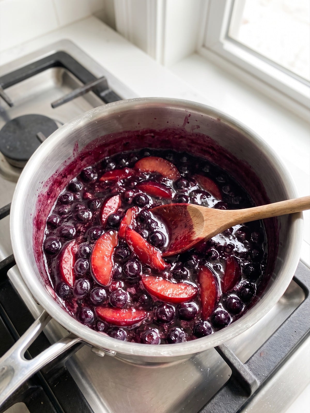 Blueberries and sliced plums simmering into a thick purple fruit sauce in a saucepan.