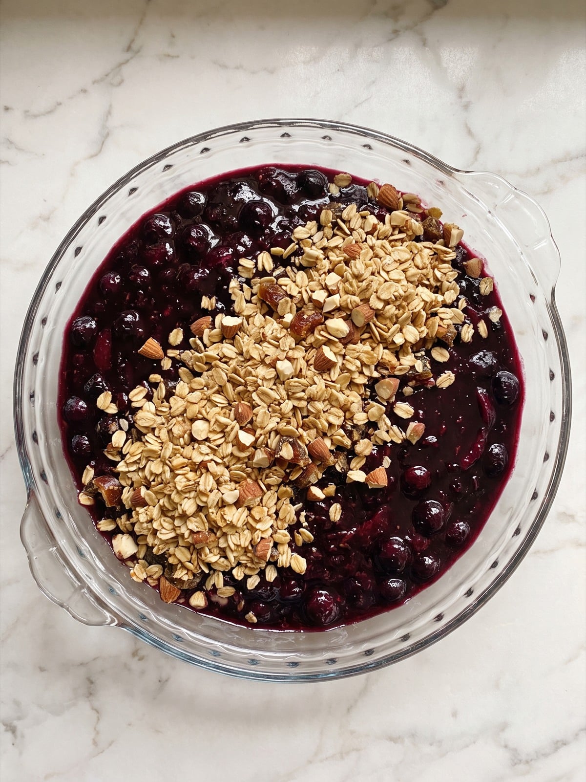 Golden oat almond crumble sprinkled over blueberry plum fruit sauce in a serving dish.