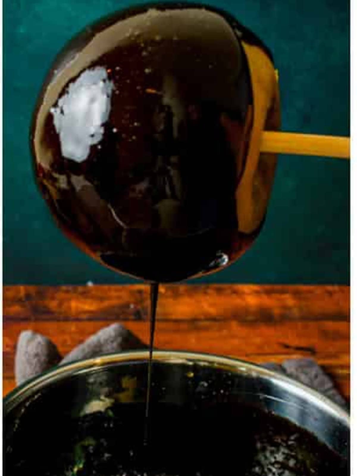 An apple being twirled in glossy black candy syrup for poison apples.