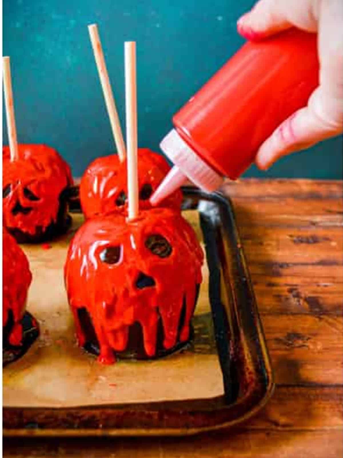 A squeeze bottle drawing spooky red candy melt faces onto black poison apples.