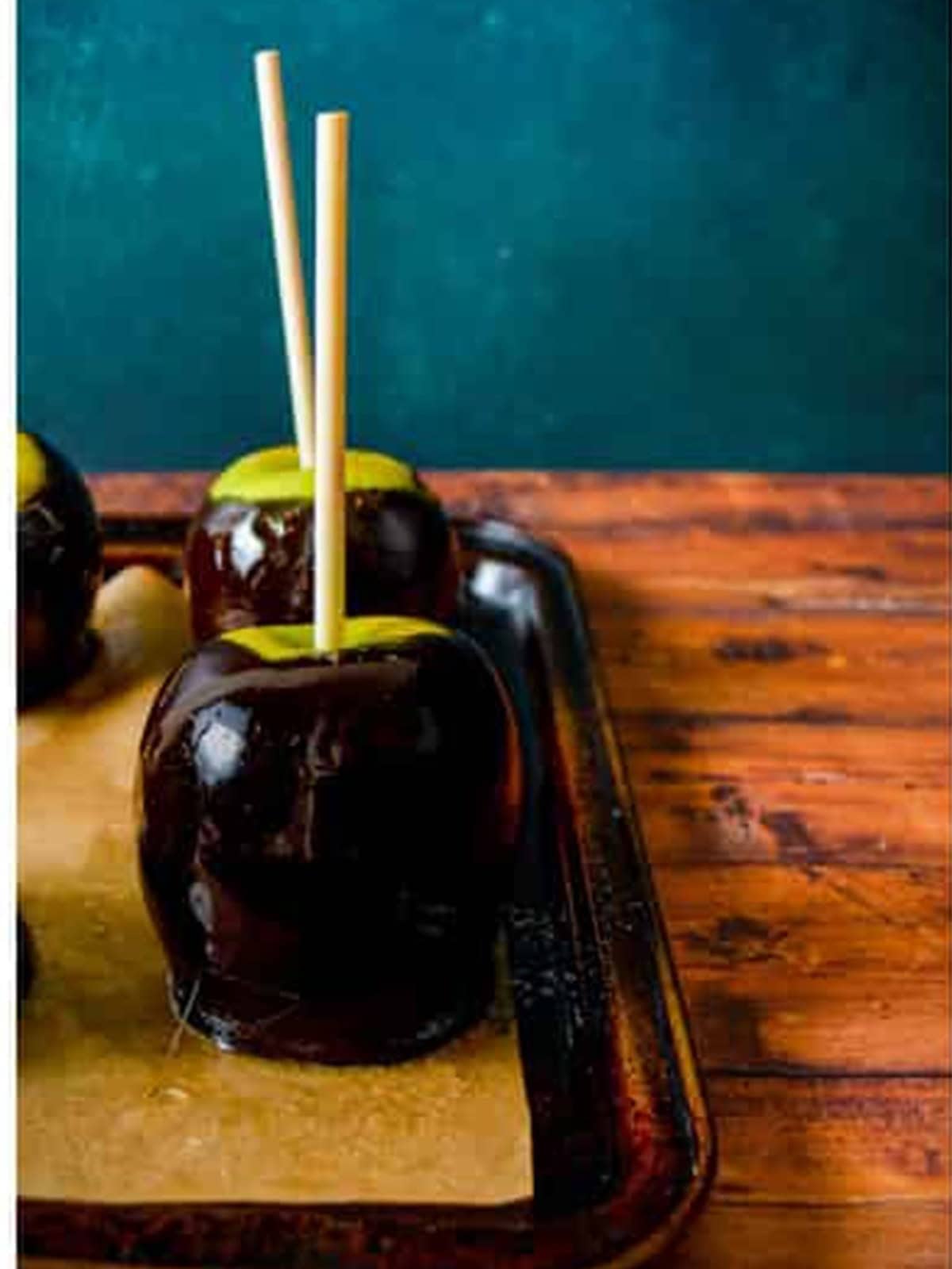 Black candy coated apples drying on parchment paper for poison apples.