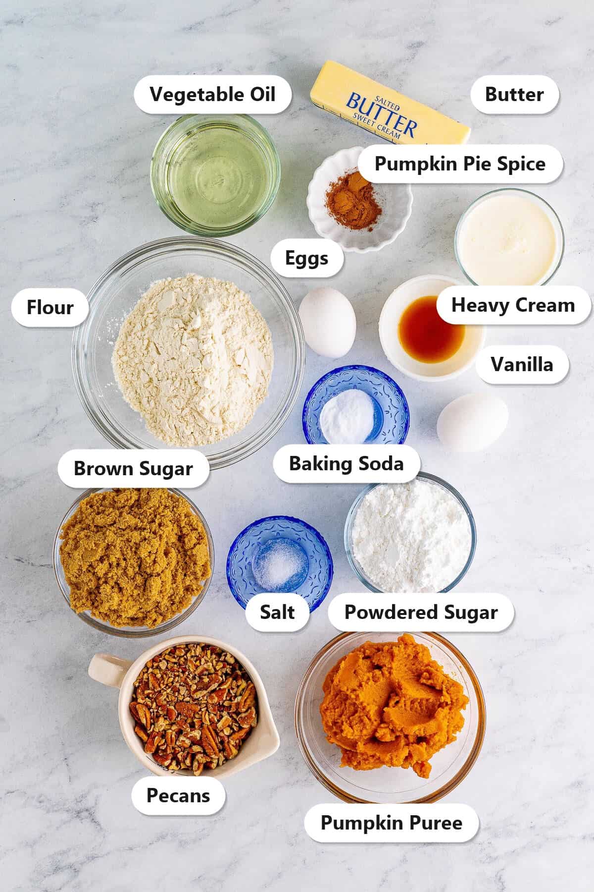 Labeled ingredients for Pumpkin Cake including flour, pumpkin puree, brown sugar, vegetable oil, eggs, butter, heavy cream, powdered sugar, pecans, vanilla, baking soda, salt, and pumpkin pie spice.