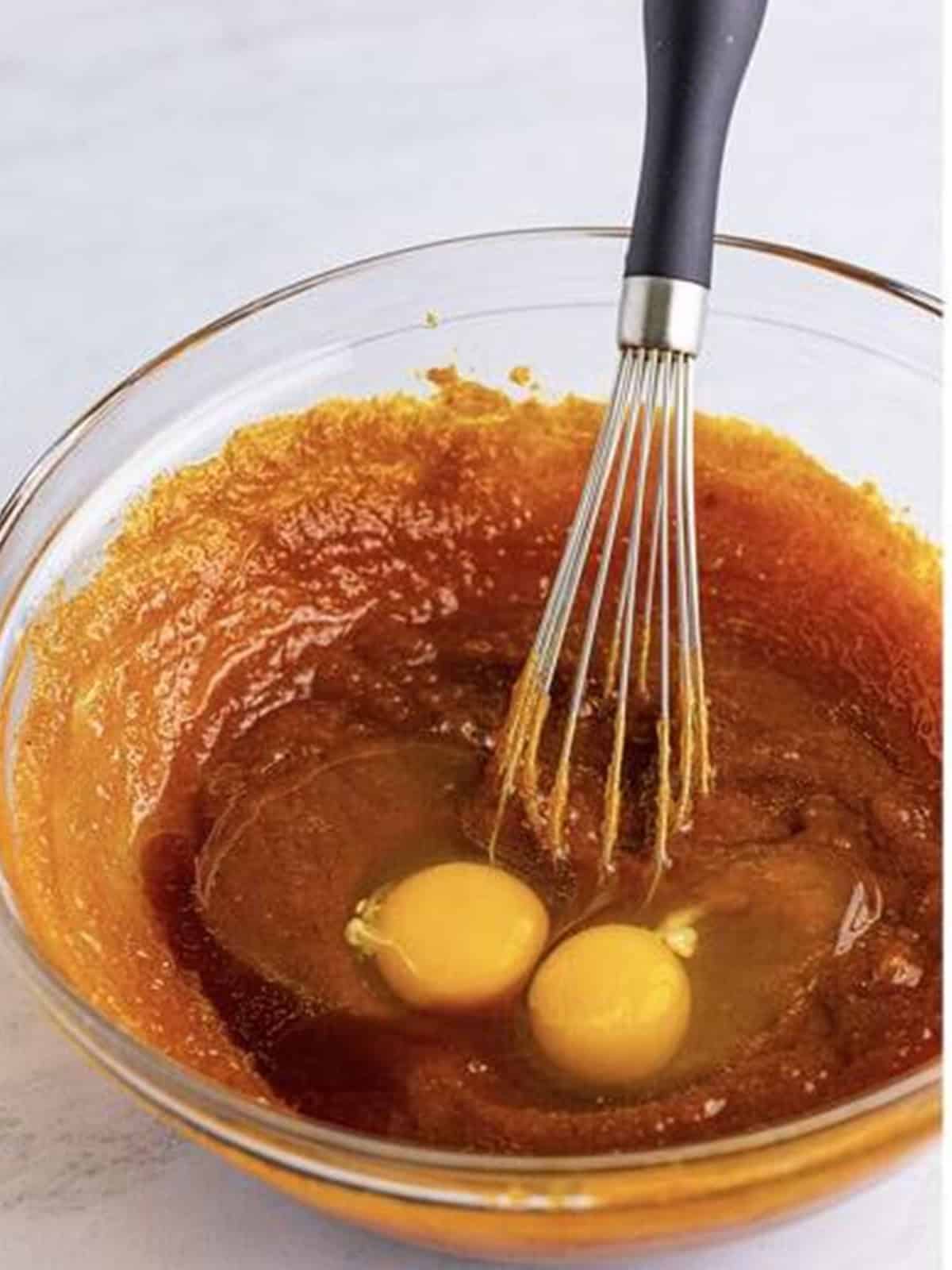 Eggs whisked into the pumpkin, brown sugar, and oil mixture in a glass bowl.