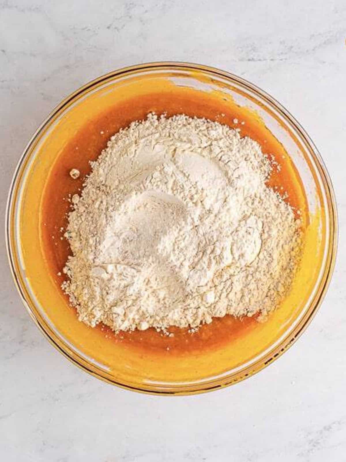 Dry ingredients added to the wet pumpkin mixture in a glass bowl.
