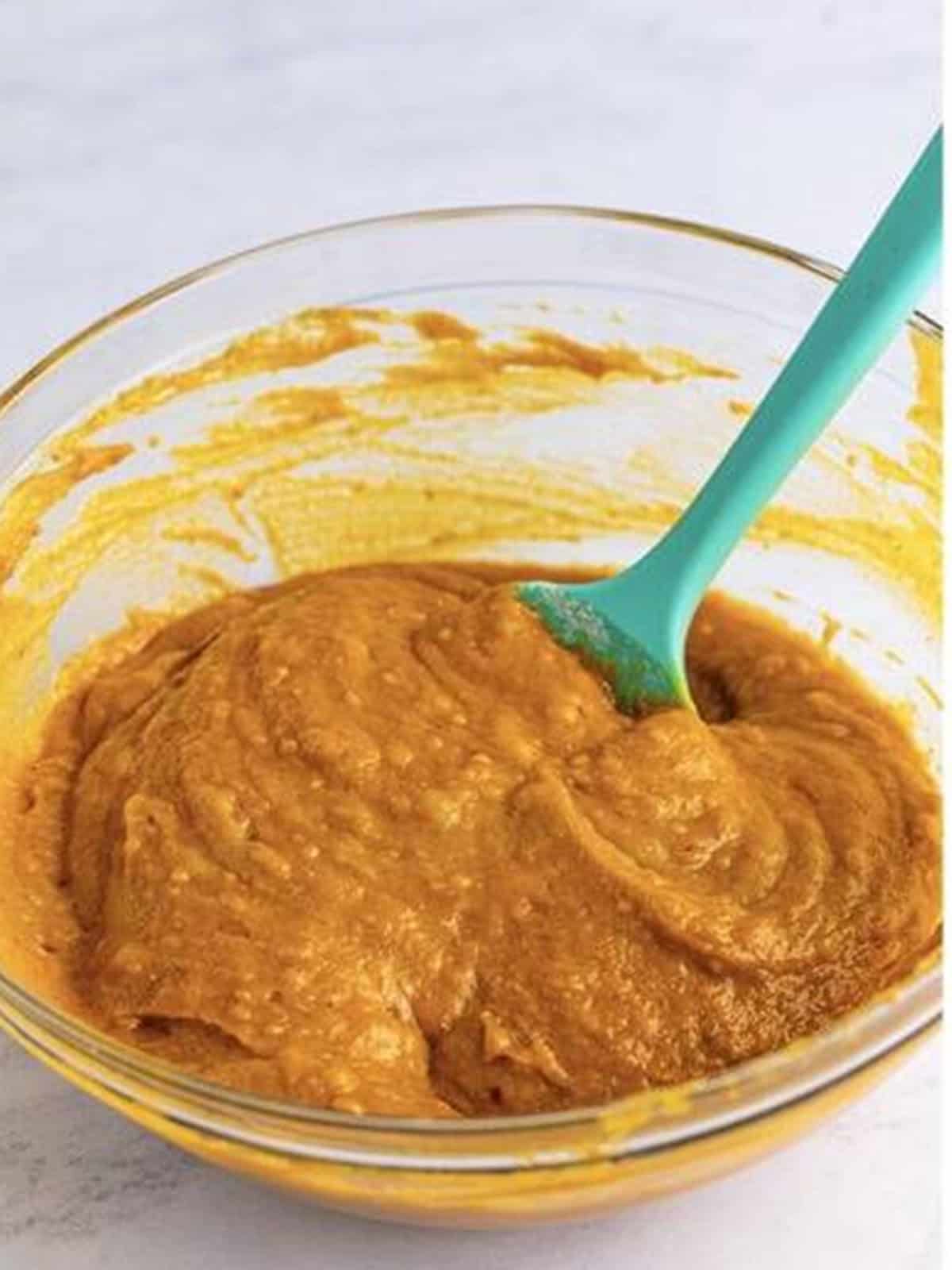 Thick pumpkin cake batter mixed with a teal spatula in a glass bowl.