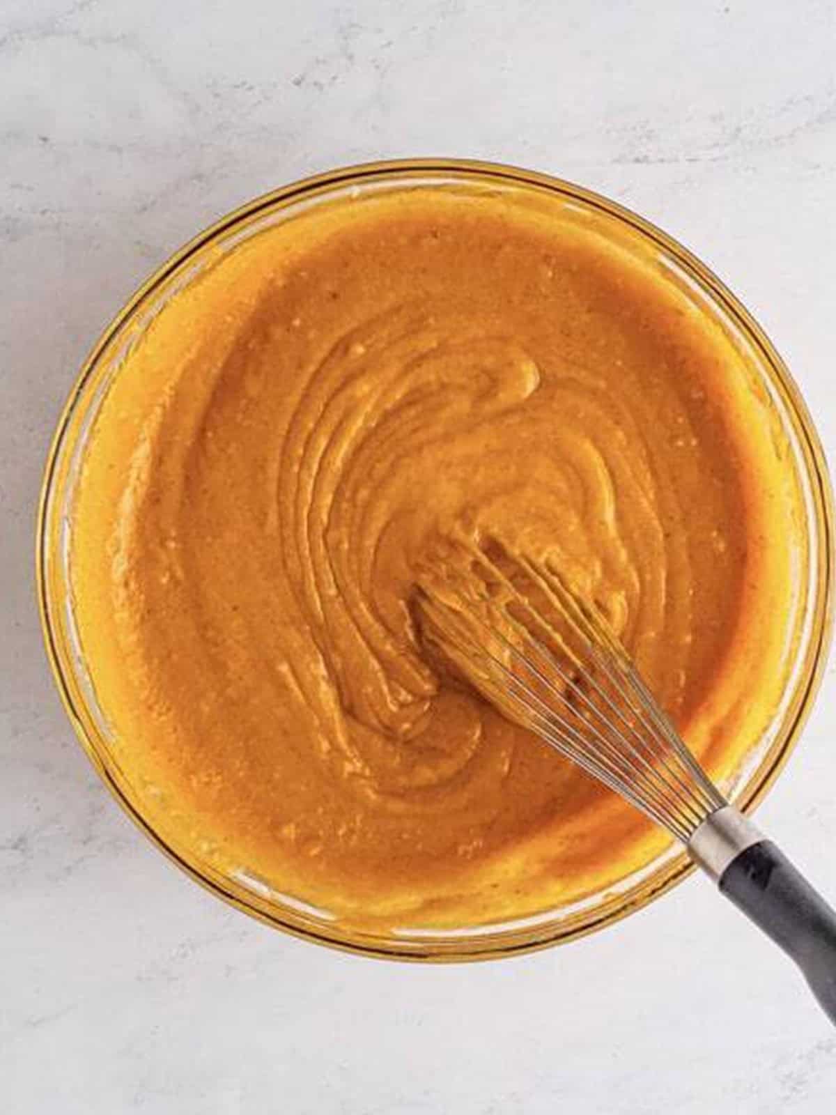 Smooth Pumpkin Cake batter whisked together in a glass bowl.