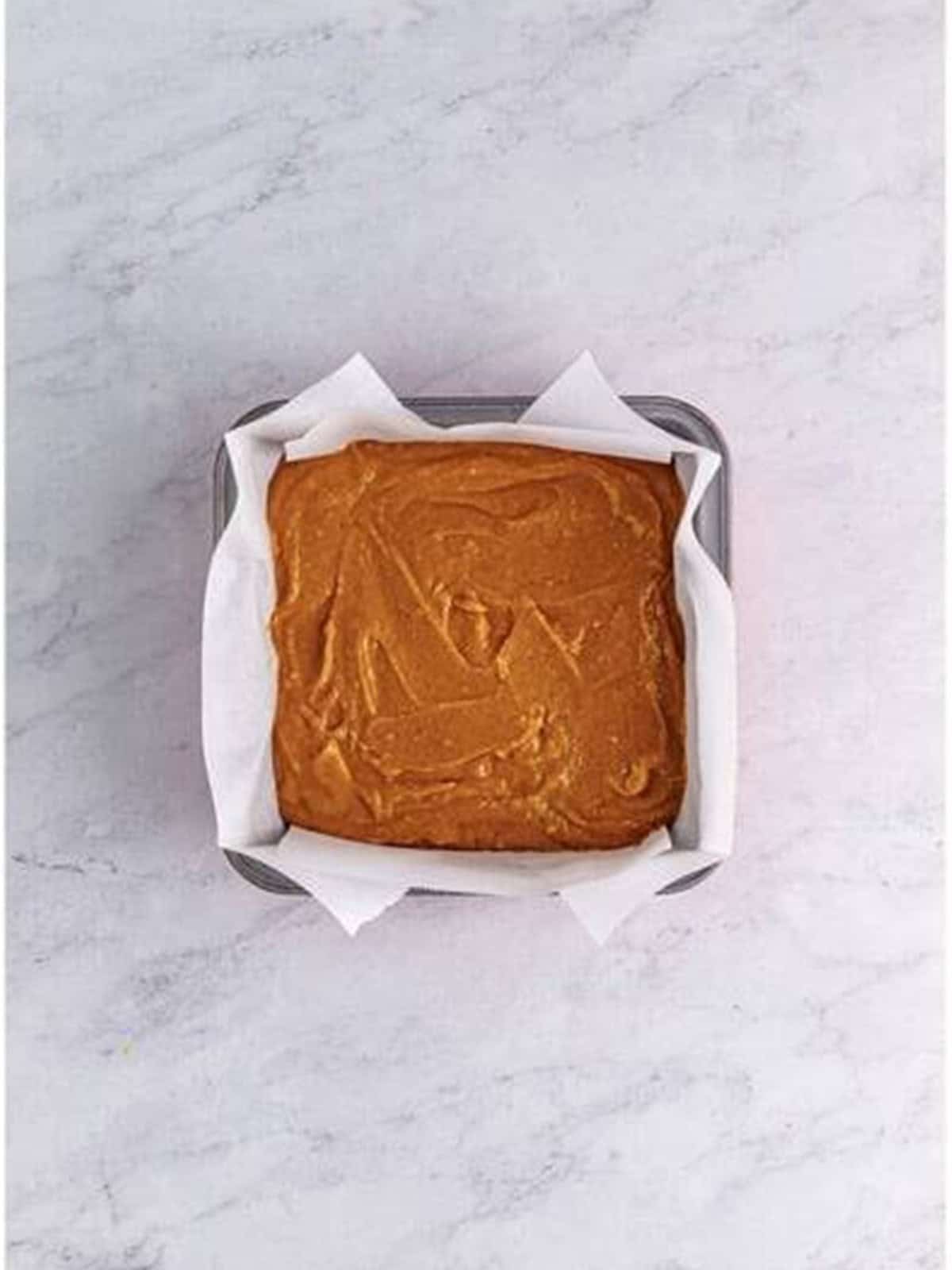 Pumpkin cake batter smoothed into a parchment lined square baking pan.