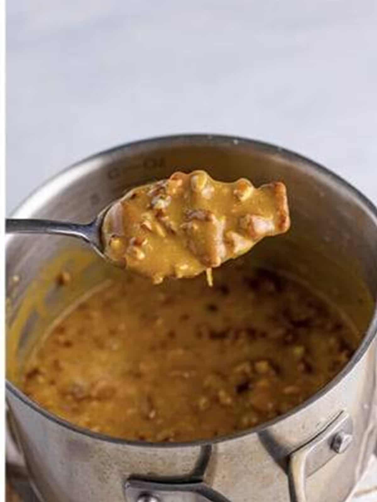 Praline frosting with toasted pecans on a spoon over a saucepan.