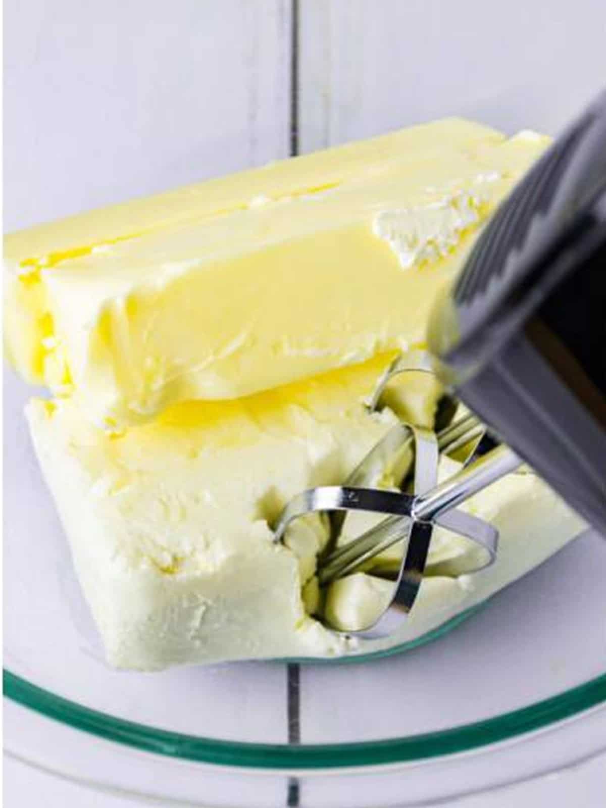 Cream cheese and butter being beaten together with a hand mixer.