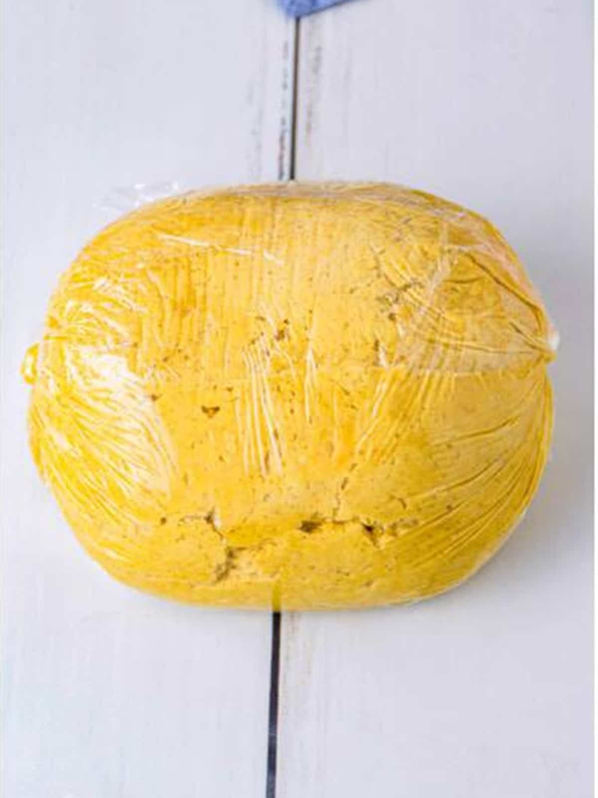 The Pumpkin Cheese Ball wrapped tightly in plastic wrap into a ball shape.