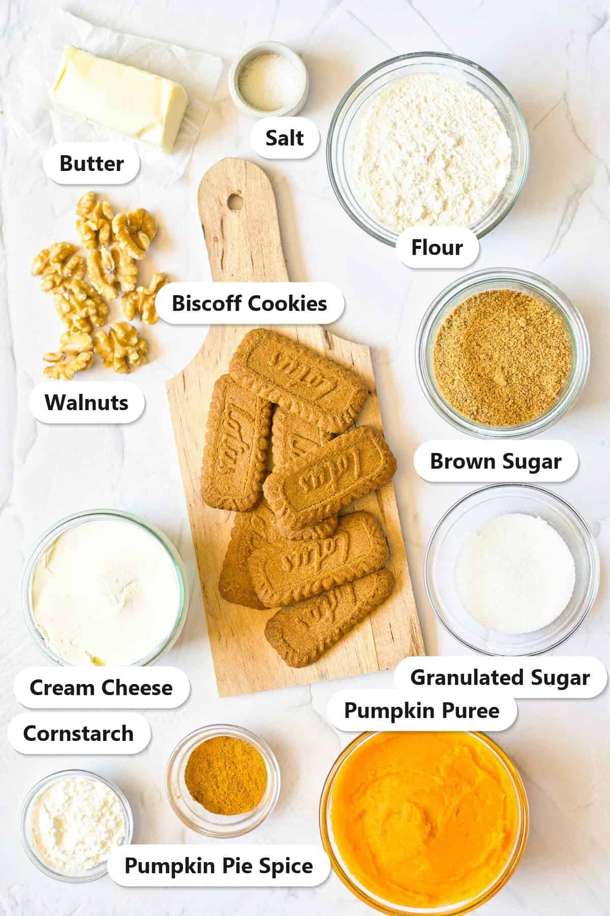 Labeled ingredients for Pumpkin Cheesecake Bars including Biscoff cookies, cream cheese, pumpkin puree, walnuts, brown sugar, granulated sugar, flour, butter, cornstarch, salt, and pumpkin pie spice.
