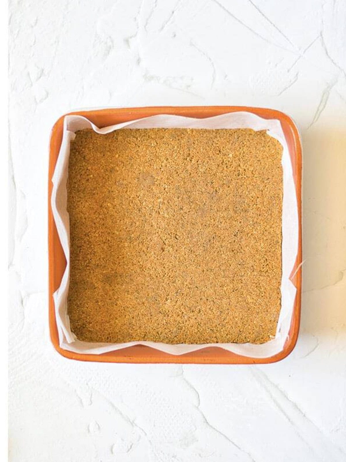 The Biscoff cookie crust pressed into a parchment lined square baking dish.