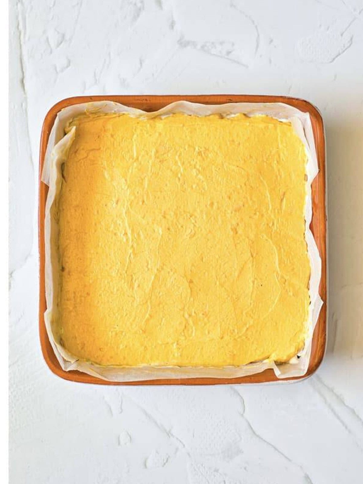The pumpkin cheesecake layer spread over the plain cheesecake layer in the baking dish.