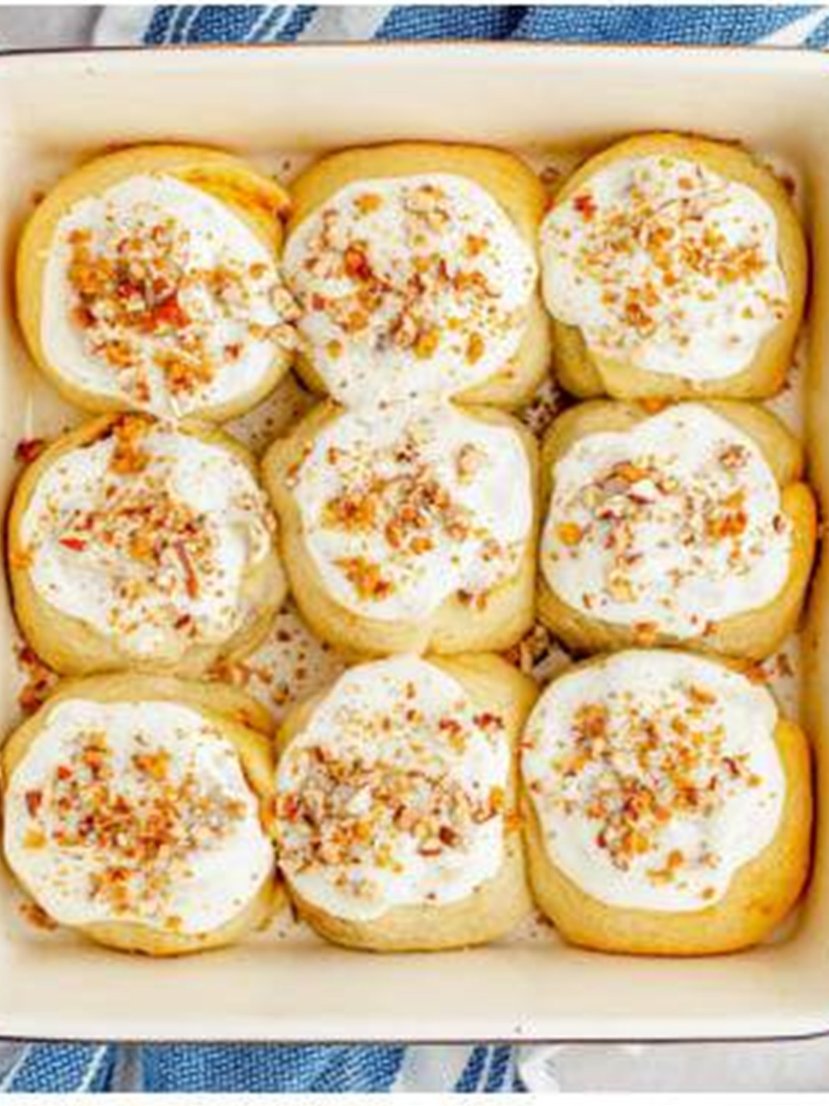 Frosted pumpkin cinnamon rolls garnished with crushed ginger snaps and pecans.
