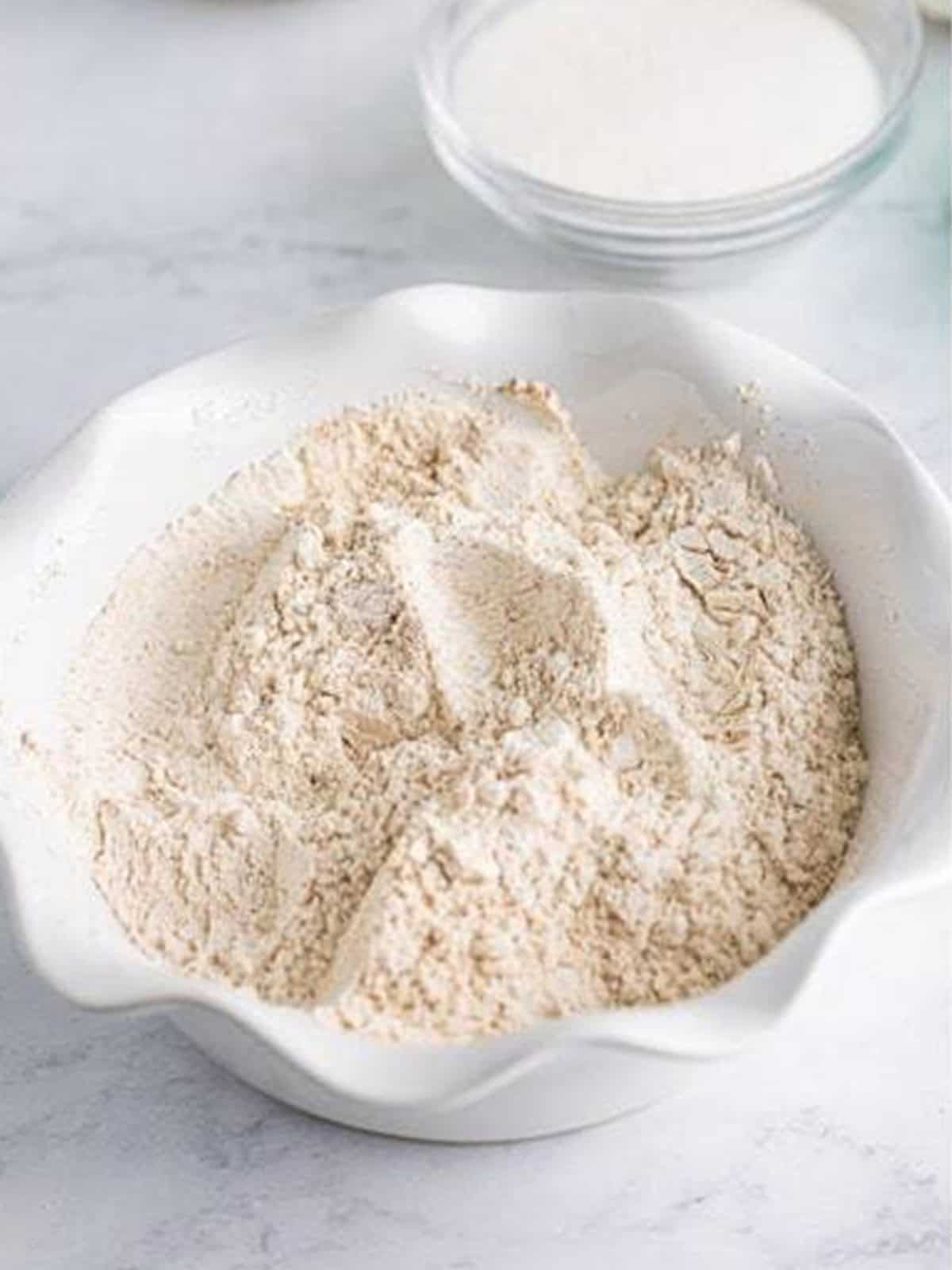 Flour, pumpkin pie spice, and baking soda stirred together in a white bowl for Pumpkin Cookies.