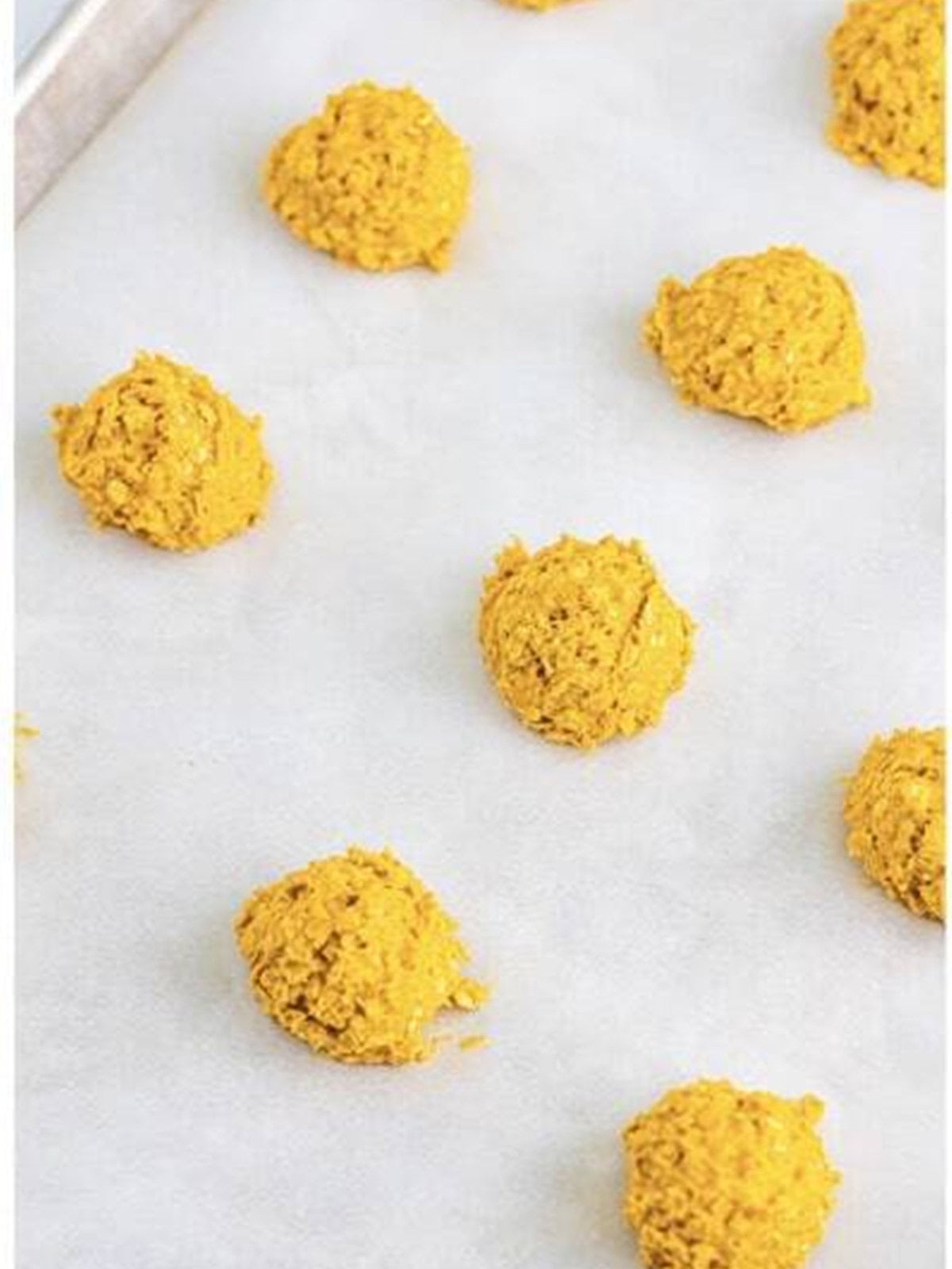 Pumpkin cookie dough scooped into balls on a parchment lined sheet tray.