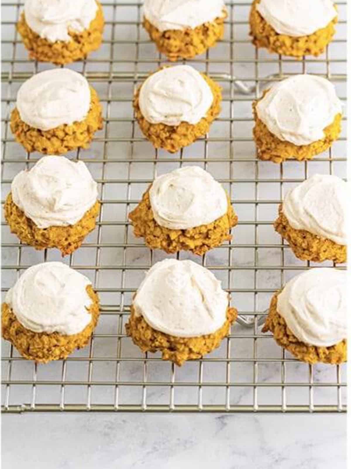 Pumpkin cookies topped with whipped frosting on a wire rack.