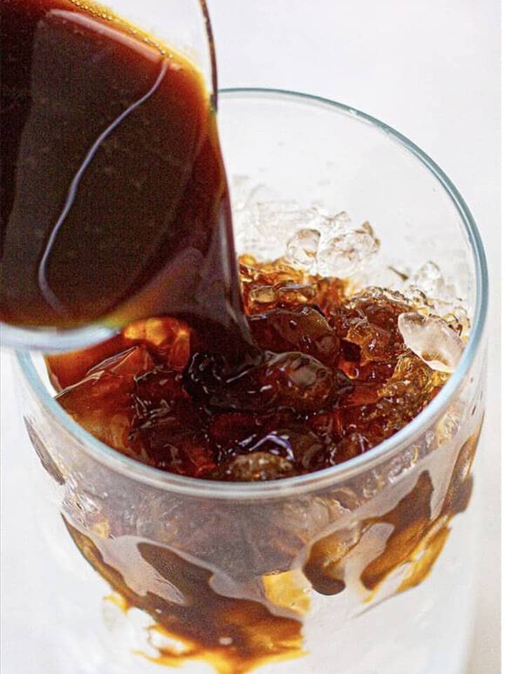 Cold brew coffee being poured over ice in a tall glass.