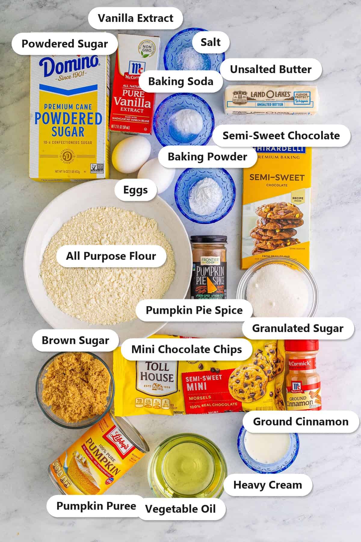 Labeled ingredients for pumpkin cupcakes: flour, pumpkin puree, pumpkin pie spice, brown sugar, eggs, mini chocolate chips, butter, semi-sweet chocolate, and more.
