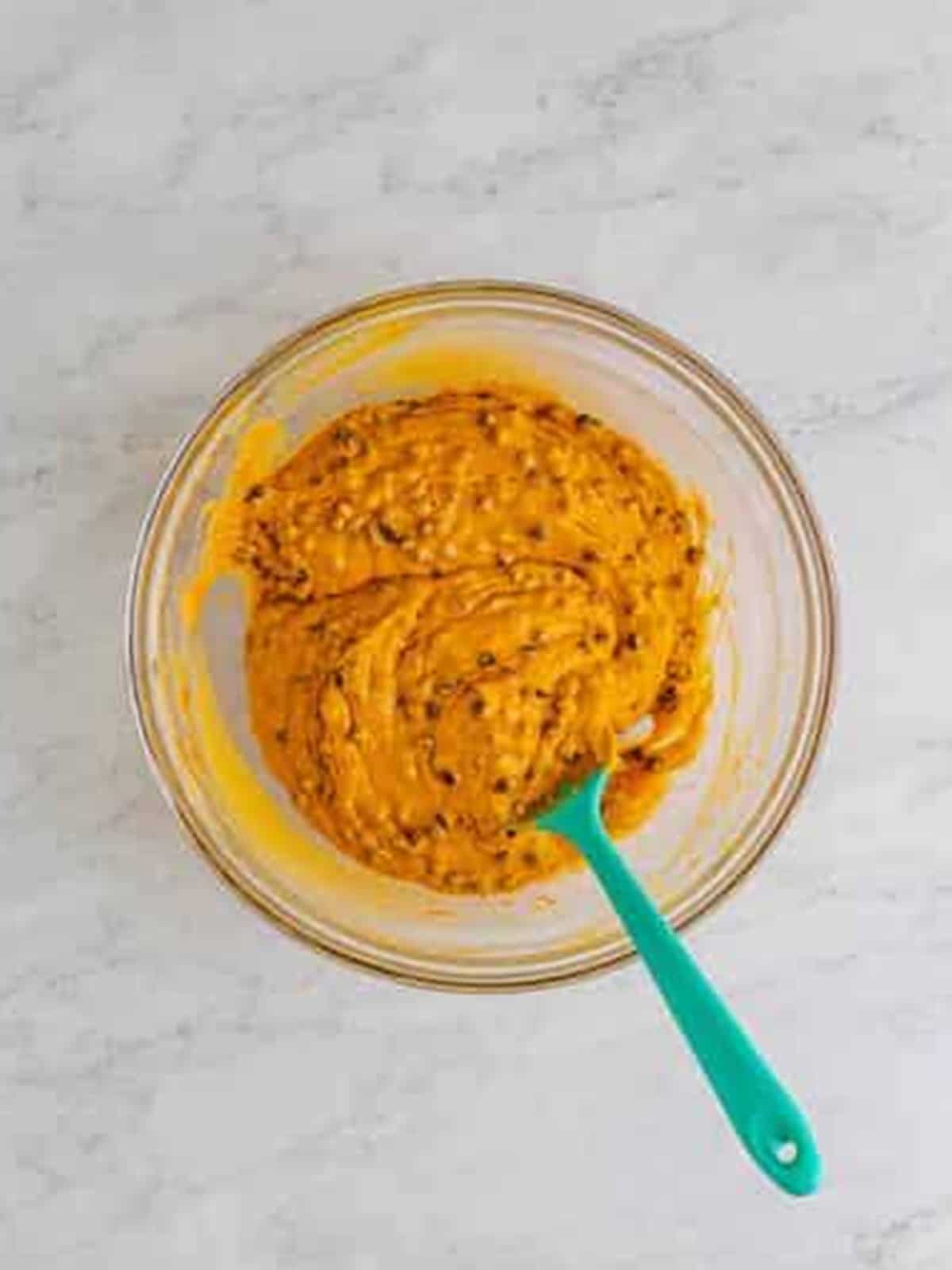 Stirring the dry ingredients and mini chocolate chips into the pumpkin cupcake batter with a spatula.