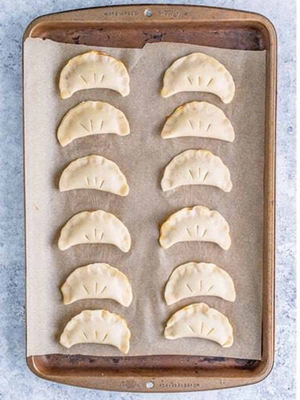Crimped Pumpkin Hand Pies with steam slits on a parchment lined tray.