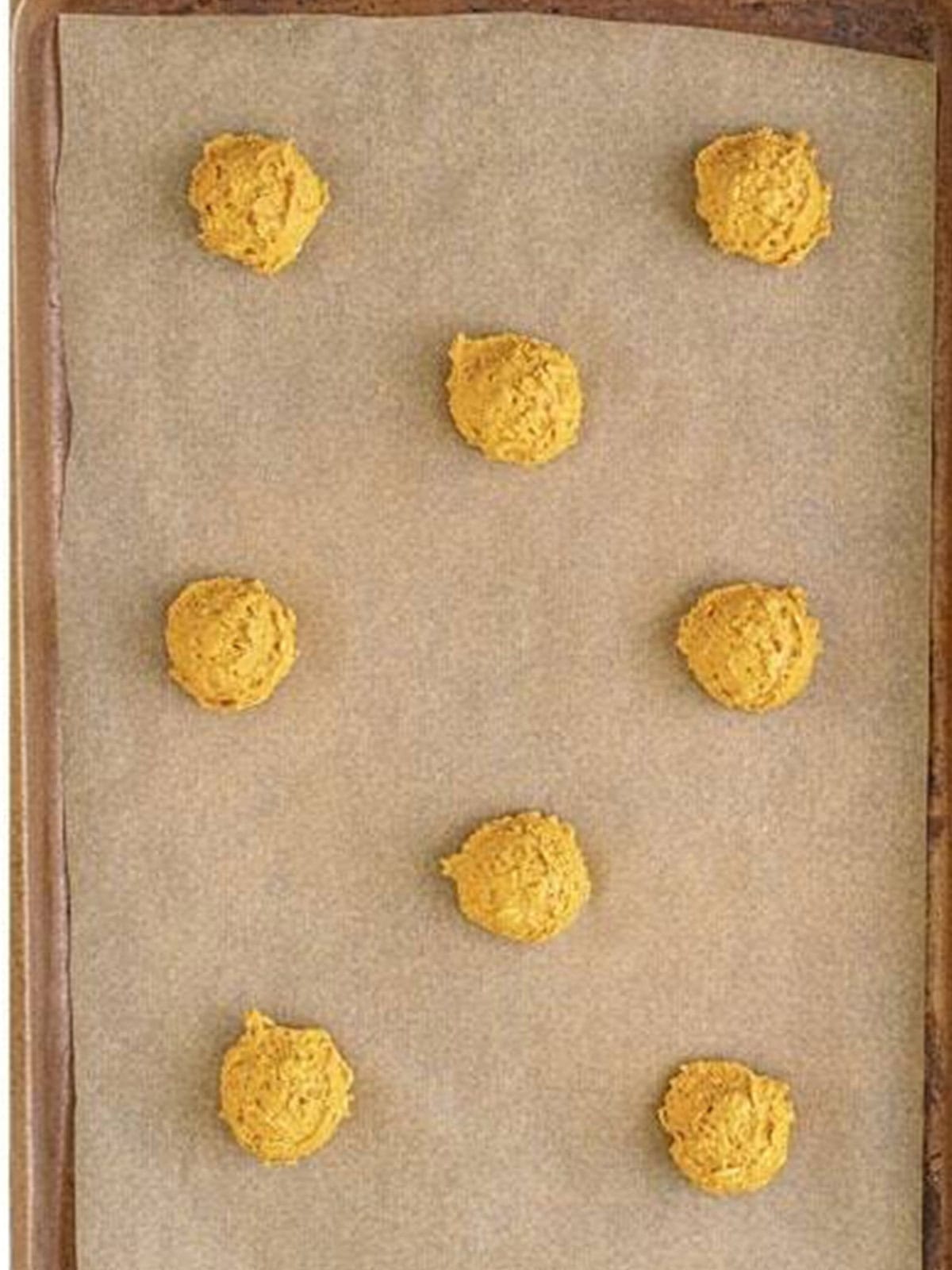 Scooped Pumpkin Oatmeal Cookies dough on a parchment lined sheet tray.