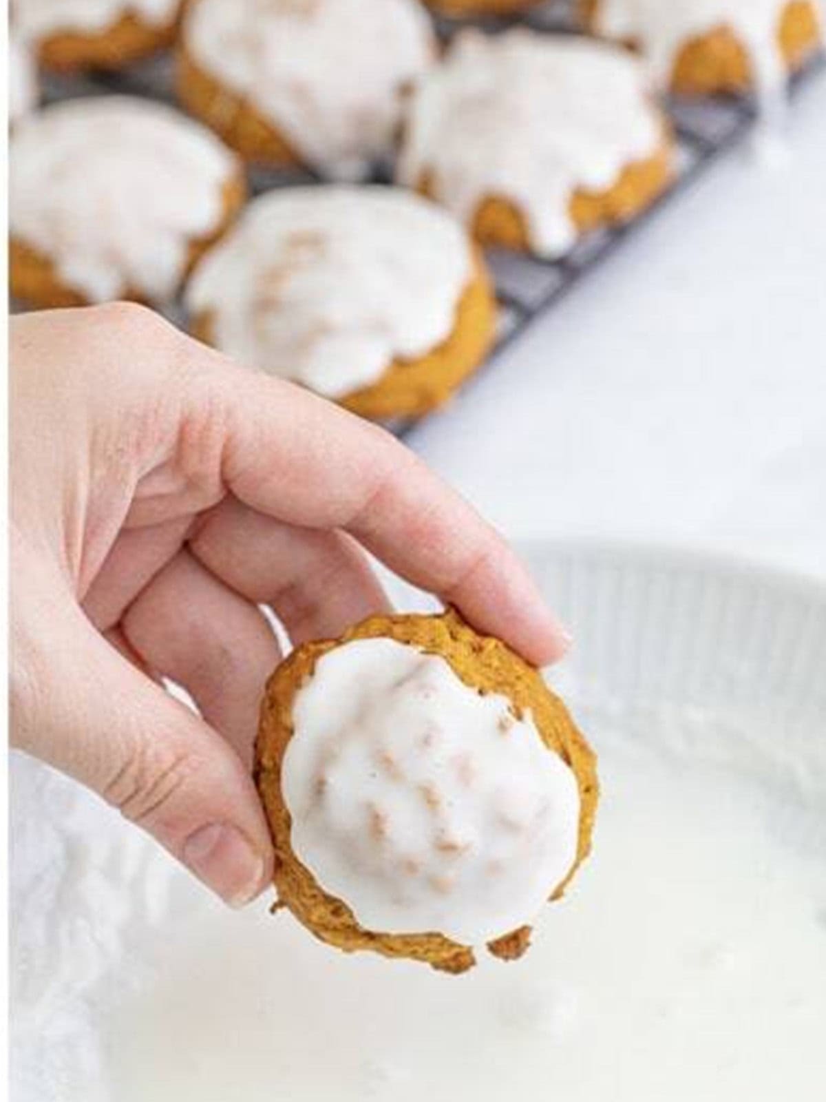 A baked pumpkin oatmeal cookie being dipped into vanilla icing.