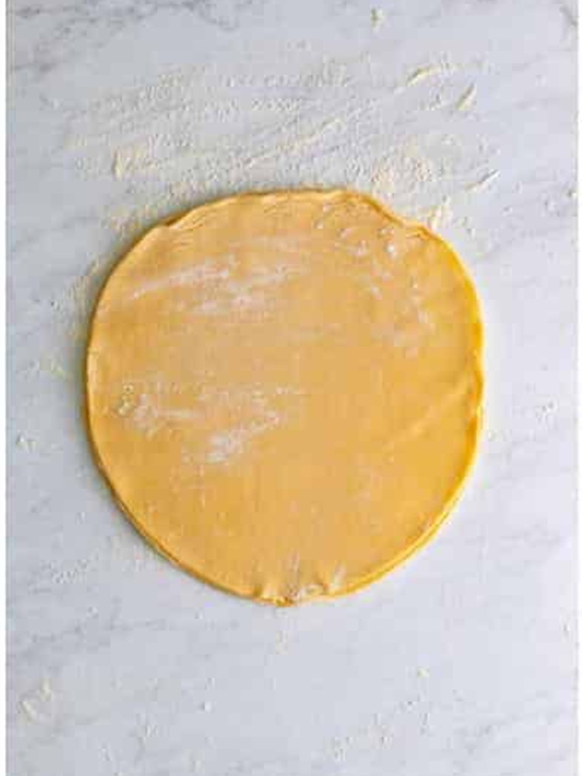 Three refrigerated pie crusts stacked and rolled together on a floured surface for pumpkin slab pie.