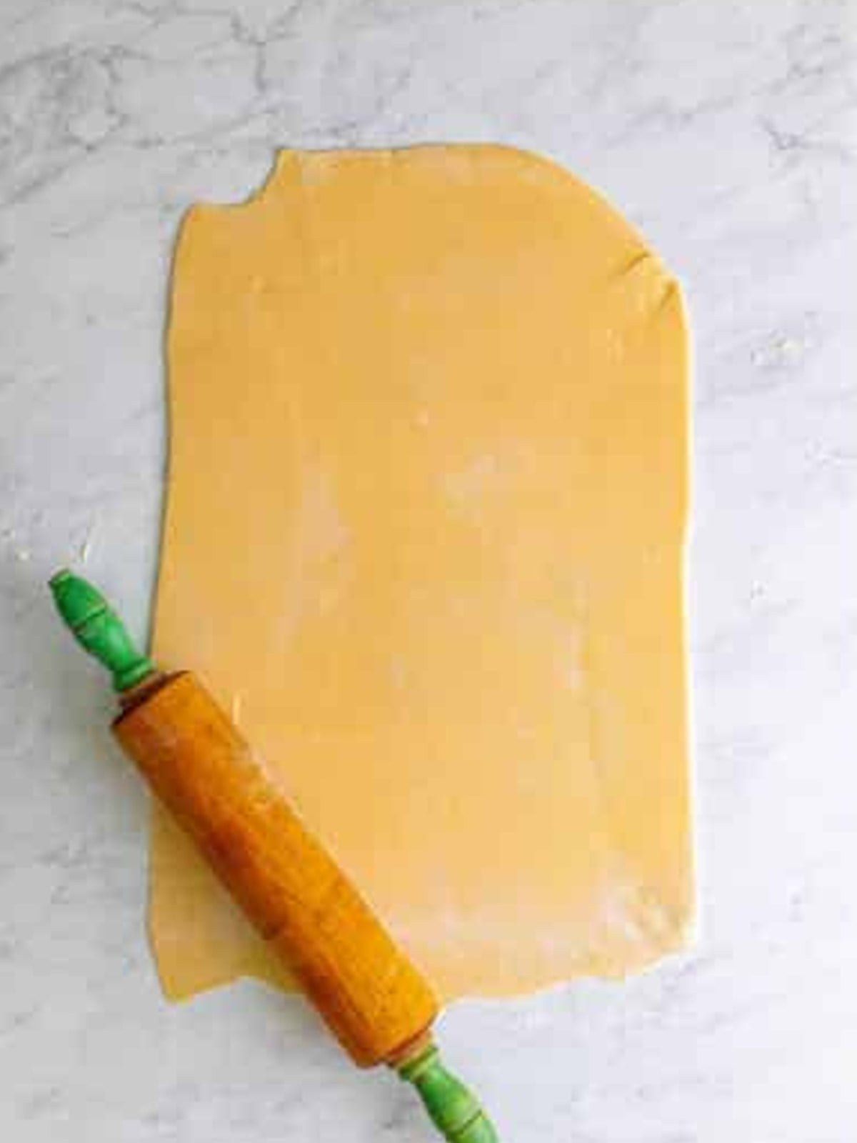 Pie crust rolled out into a large rectangle with a rolling pin for pumpkin slab pie.