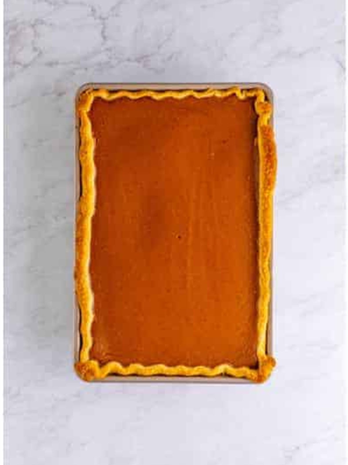 Baked pumpkin slab pie cooling in the jelly roll pan with a golden crimped crust.